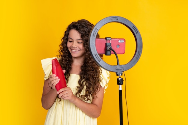Blogger-beïnvloeder voor tienermeisjes houdt haarconditioner of shampoofles vast en gebruikt selfie led-lamp