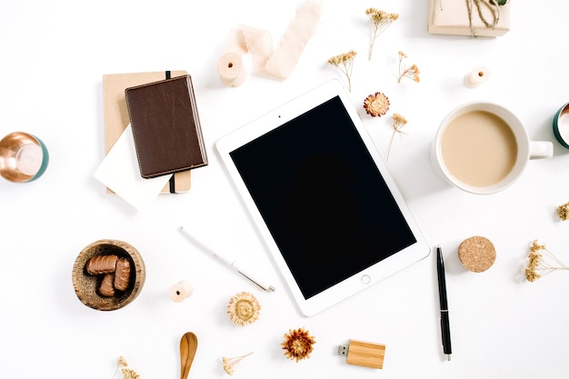 Blogger or freelancer workspace with tablet, coffee mug, notebook, sweets and accessories on white background. Flat lay, top view minimalistic brown styled home office desk. Beauty blog concept.