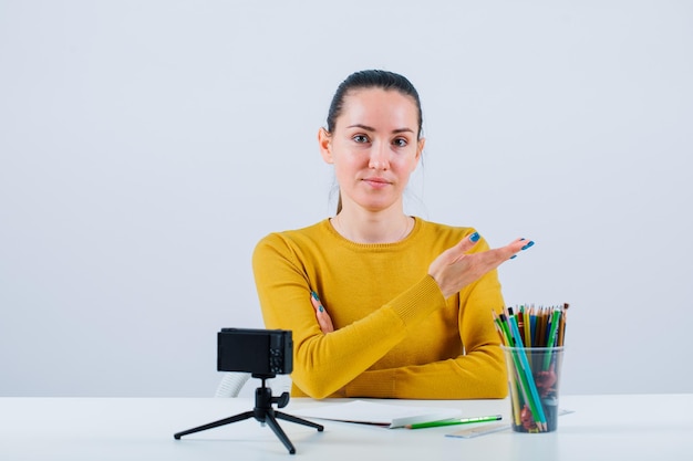 Blogger girl is pointing right with hands by sitting on white background