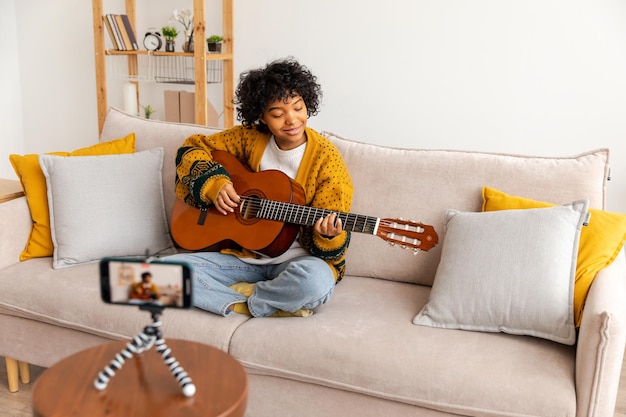 ブロガー ギタリスト アフリカ系アメリカ人の女の子のブロガーがギターを弾き、ウェブカメラの録音 vlog soci と話している