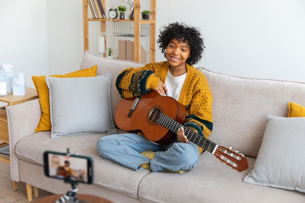 ブロガー ギタリスト アフリカ系アメリカ人の女の子のブロガーがギターを弾き、ウェブカメラの録音 vlog soci と話している