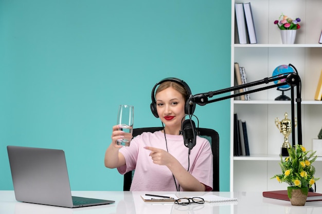 Blogger journalist pretty cute blonde girl recording video on computer holding glass