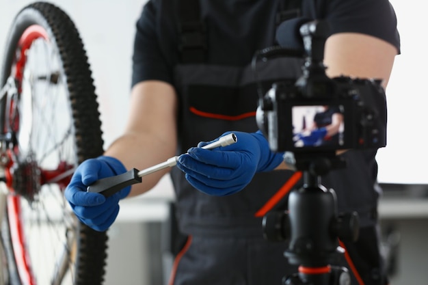 Blogger mechanic fix bicycle in workshop busy young worker in shirt and gloves