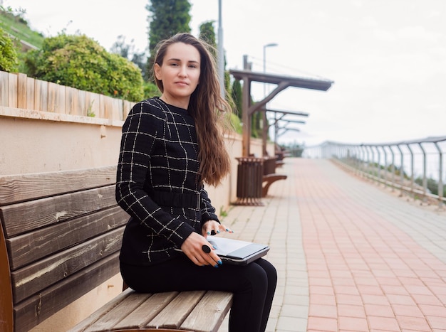 Blogger-meisje met een computer zit op een bankje in het park