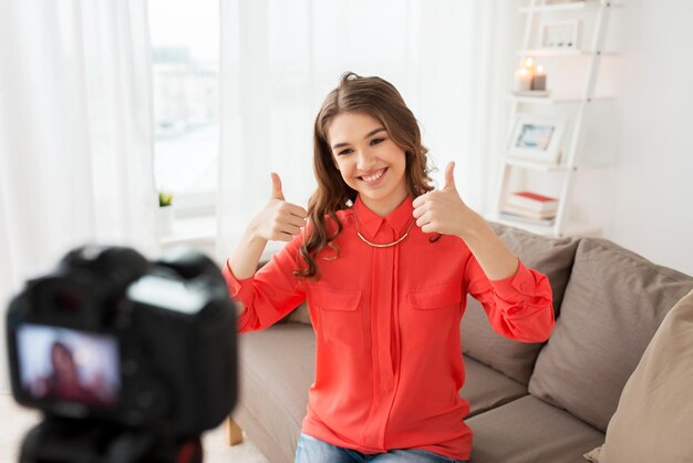 Foto blogging, tecnologia, videoblog, mass media e concetto di persone - felice donna sorridente o blogger con videocamera che registra video e mostra i pollici in su a casa