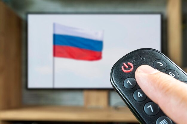 Blokkering van Russische tv-uitzendingen Afstandsbediening in de hand van een man op de achtergrond van een tv en een Russische vlag Het concept van het loskoppelen van Russische kanalen in Europa en de VS