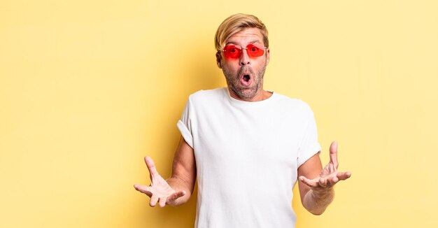 Blond adult man amazed, shocked and astonished with an unbelievable surprise and wearing sunglasses