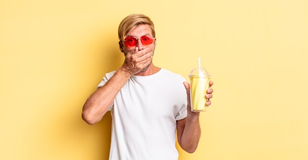 blond adult man covering mouth with hands with a shocked with a milkshake