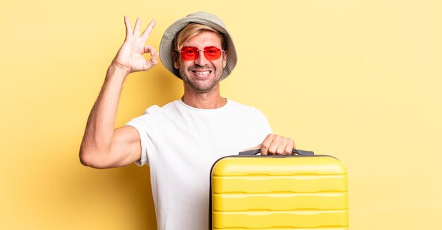 Blond adult man feeling happy, showing approval with okay gesture. traveler concept