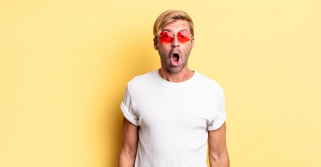 Photo blond adult man looking very shocked or surprised and wearing sunglasses