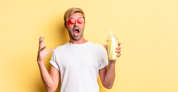 Blond adult man screaming with hands up in the air with a milkshake