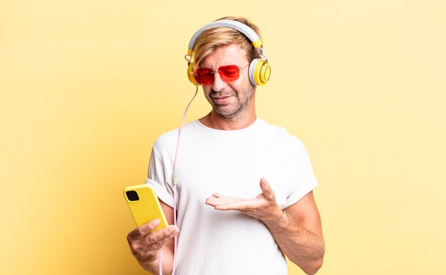 blond adult man smiling cheerfully, feeling happy and showing a concept with headphones