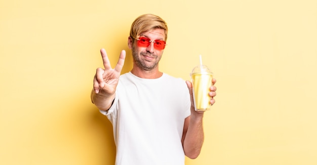 Blond adult man smiling and looking friendly, showing number two with a milkshake