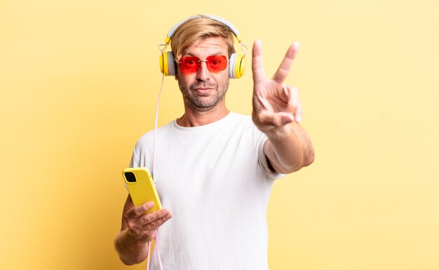 Blond adult man smiling and looking happy, gesturing victory or peace with headphones