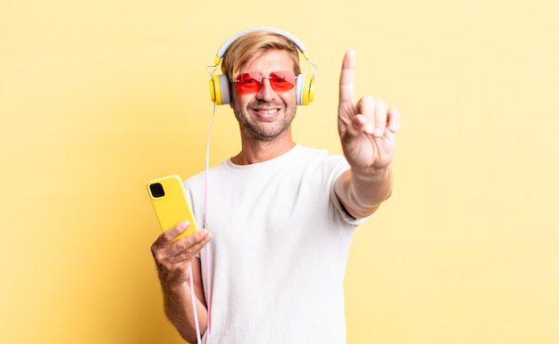 Blond adult man smiling proudly and confidently making number one with headphones