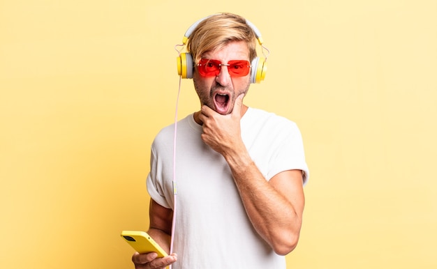 Blond adult man with mouth and eyes wide open and hand on chin with headphones