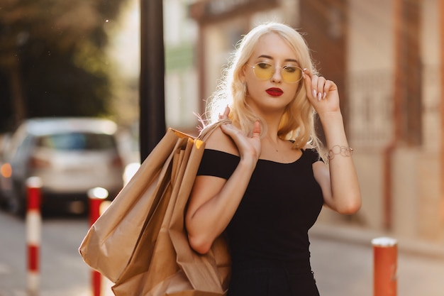 Blond attractive girl in sunglasses after shopping in summer sunshine