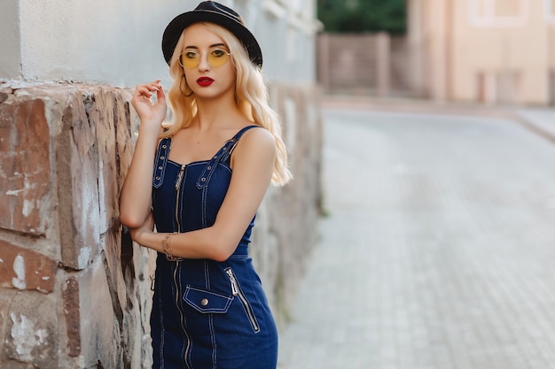 Blond attractive girl in sunglasses and stylish hat at summer sunshine urban