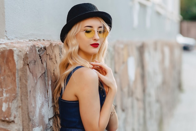 Blond attractive girl in sunglasses and stylish hat at summer sunshine urban