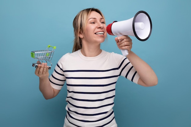 Blond attractive young woman in casual attire speaks using a megaphone while holding a supermarket