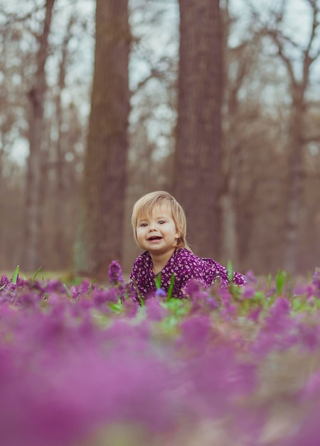 blond baby in a colored dress lies in a forest glade in flowers