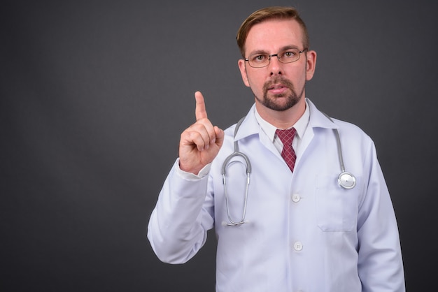 Blond bearded doctor with goatee against gray wall