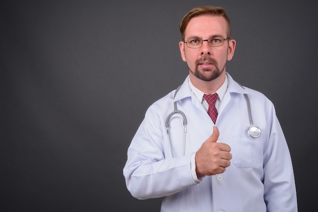 Blond bearded doctor with goatee against gray wall