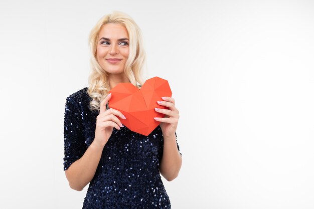 Blond beautiful girl in a blue dress holds valentines from paper in the form of a heart on a white with copy space