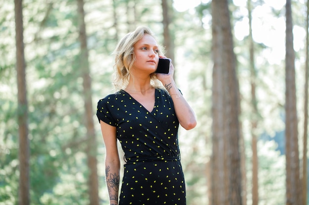 Foto blond bloggermeisje praat op mobiel door weg te kijken op de achtergrond van de natuur