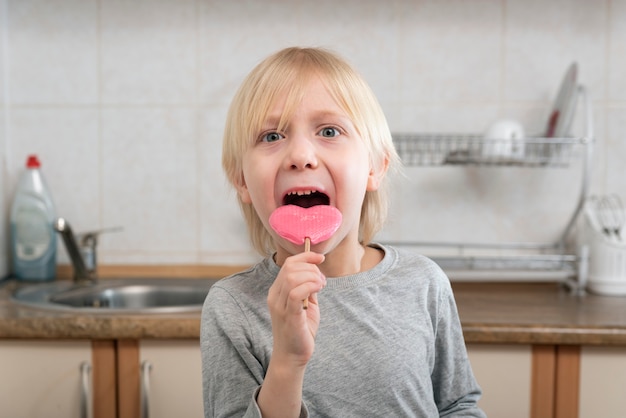 ハート型のピンクのロリポップを食べる金髪の少年