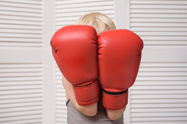 Blond boy is protected in two boxing gloves. Portrait