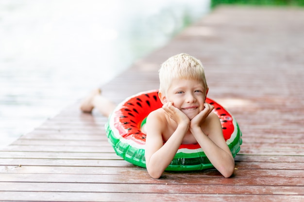 金髪の少年は夏に円で湖の近くの桟橋にあります。