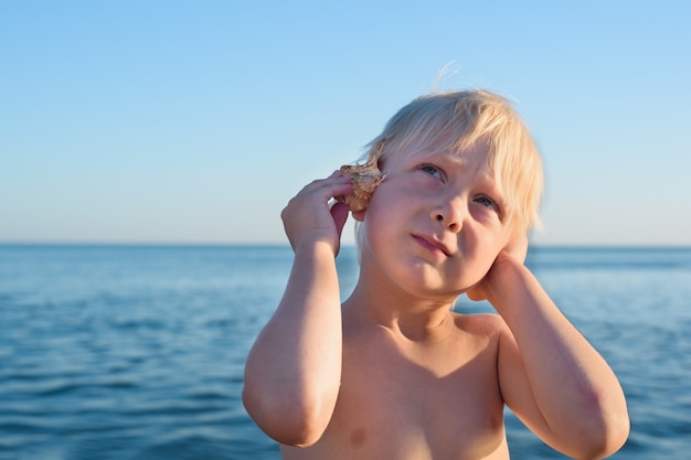 Blond boy listens to the sea in shell.