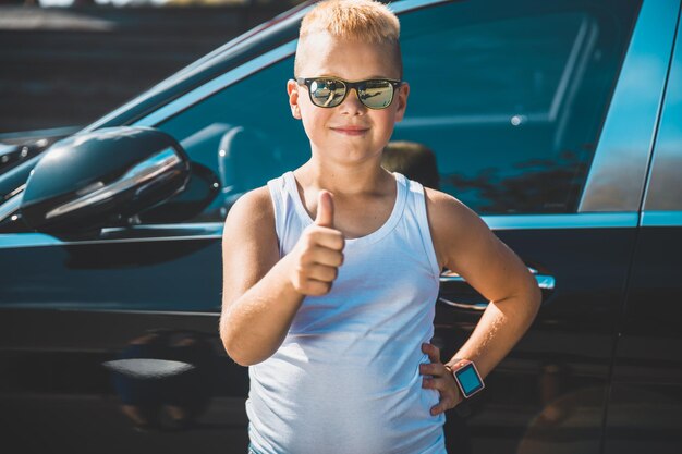 Blond boy shows thumb on the background of the car