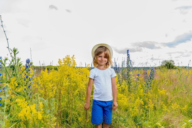 A blond boy in a straw hat stands among the wildflowers