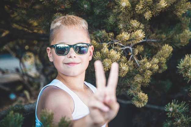 Blond boy in sunglasses shows two fingers.