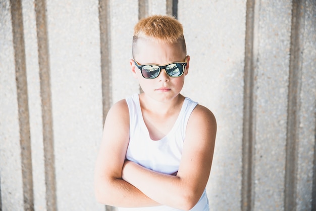 Blond boy in sunglasses stands against the wall