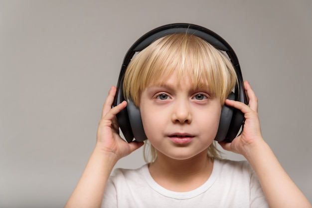 Blond boy teenager with headphones on light wall. Teenager listens to music. Portrait