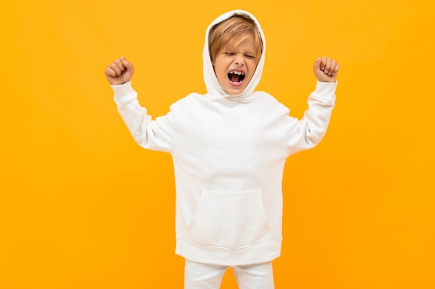 blond boy in a white hoodie screaming out loud on orange wall