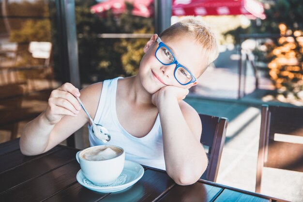 Blond boy in a white t-shirt in a restaurant drinking coffee