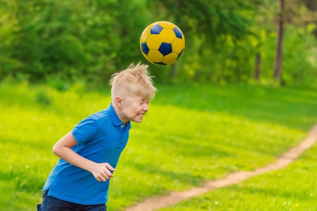 Blond boy in a white tshirt boy beats his head a soccer ball in the park