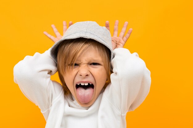 Blond boy with panama grimaces on yellow studio