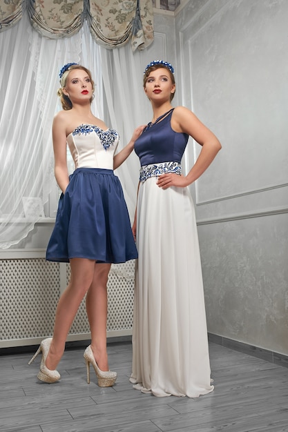 Blond, brunette women posing in blue and white dresses