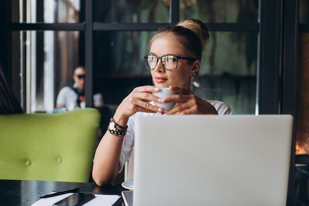 Фото Блондинка деловая женщина сидит на рабочем месте и с помощью ноутбука в офисе, она смотрит на папку с документами, разговаривает по телефону и пить чашку кофе.