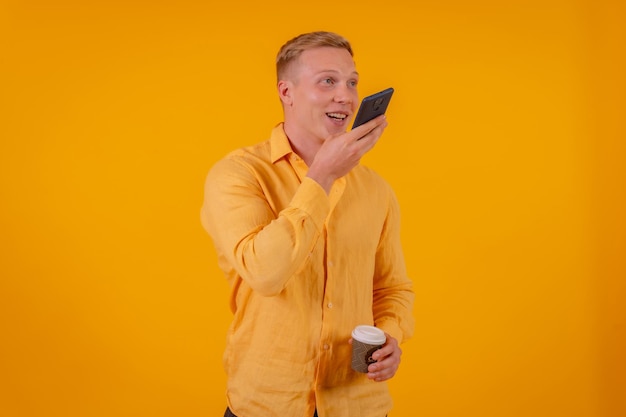 Blond caucasian man on a yellow background sending a voice note smiling