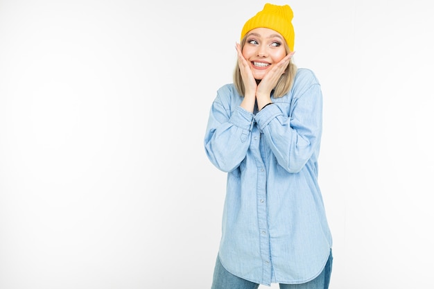 Blond charmant meisje in een casual look met een spijkeroverhemd omhelst zichzelf op een witte achtergrond.