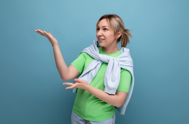 Blond cheerful bright girl in a casual outfit shows her hand at a banner on a blue background with