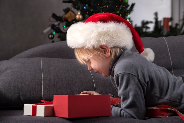 Blond child in Santa hat looks into an open gift box. Christmas and New Year.