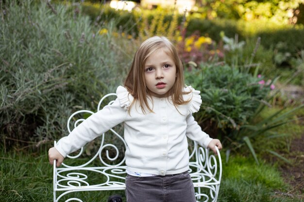 Blond cute girl near the bush on bench in summer