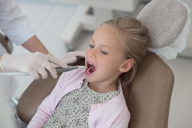 A blond doctor holding a dental drill while working with her little patient